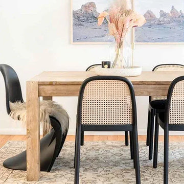 Modern dining table with black cane chairs, rustic wood finish, and boho rug in stylish home decor setting
