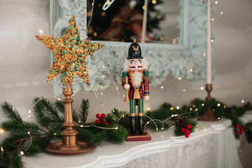 Festive nutcracker figurine on mantel with glitter star, pine garland, and fairy lights for holiday home decor