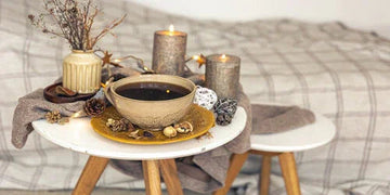 Cozy home decor with rustic candles, dried flowers, and a warm drink on a wooden side table.