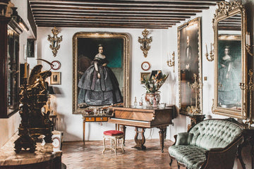 Elegant vintage living room with antique piano, ornate gold-framed portraits, tufted velvet sofa, and classic decor accents.