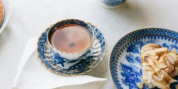 Blue and white porcelain teacup with gold trim, served with almond pastry on matching plate, elegant tea setting
