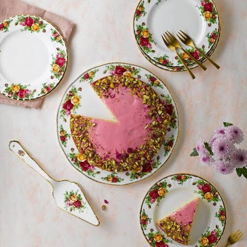 Floral ceramic plates with pink pistachio cake, gold forks, and purple flowers for elegant home dining decor