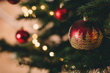 Red Christmas ornament with gold tree design on a festive tree with warm lights