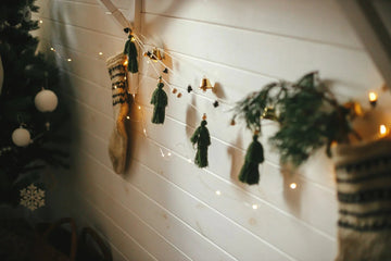 Cozy Christmas decor with tassel garland, fairy lights, and stockings on white shiplap wall