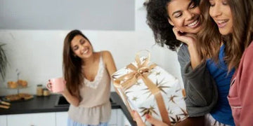 Women celebrating with a stylish gift box in a cozy kitchen setting