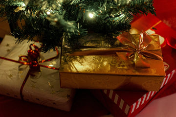 Festive Christmas gifts wrapped in gold and red under a lit tree, perfect for holiday home decor.