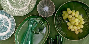 Green ceramic plates with floral patterns, grapes, and glassware on a table