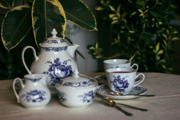 Elegant blue floral tea set with teapot, cups, saucers, and sugar bowl on table, styled with lush green plants for home decor.
