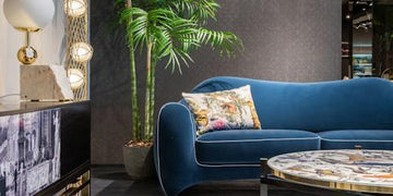 Luxury blue velvet sofa with tropical pillow, modern side table, and palm plant in stylish living room decor