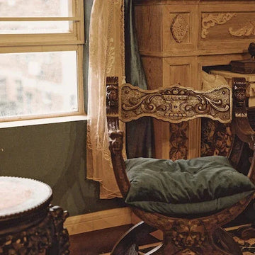 Ornate wooden chair with green cushion near window, vintage home decor style