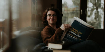 Woman reading career fair brochure on cozy couch near window
