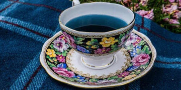 Floral porcelain teacup with blue tea on plaid blanket, garden setting