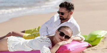 Couple relaxing on colorful beach floaties by ocean waves, stylish summer vacation scene