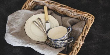 Woven basket with vintage plates, blue floral teacup, and cutlery on linen napkin for home decor
