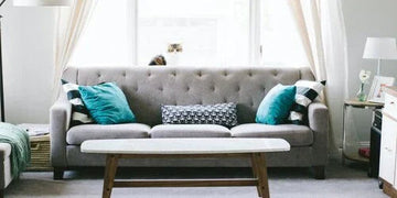 Gray tufted sofa with teal and patterned pillows in a bright living room