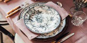 Elegant floral-patterned dinnerware set on a rustic table with woven placemat and bamboo cutlery
