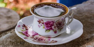 Elegant floral teacup with roses, filled with coffee, set on stone surface for cozy home decor