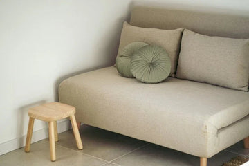 Beige fabric sofa with green pleated cushion and wooden side stool in minimalist living room