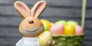 Smiling ceramic bunny holding polka dot egg with colorful Easter eggs in basket