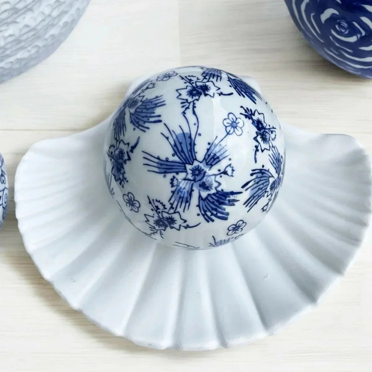 Blue and white ceramic decorative ball with floral pattern on a white shell dish, home décor