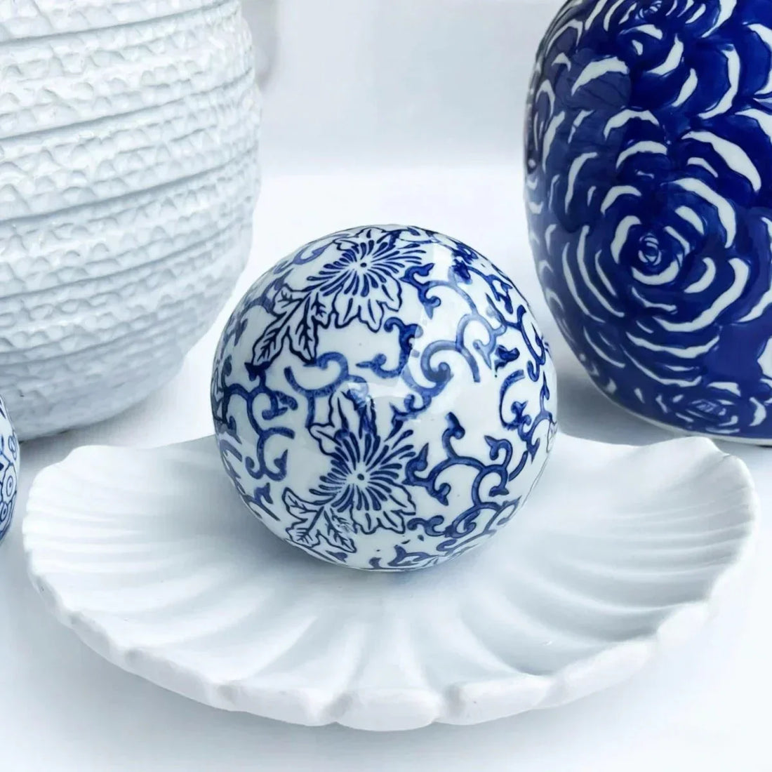 Blue and white decorative ceramic ball on shell-shaped dish, elegant home décor accent.