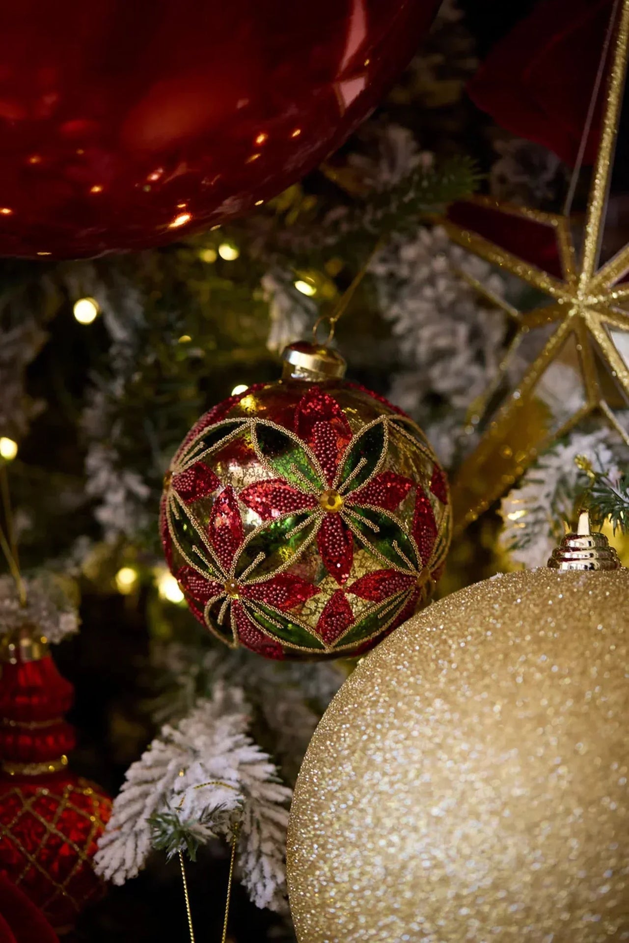Red and green beaded Christmas ornament on flocked tree with gold glitter baubles