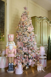 Pink and gold flocked Christmas tree with floral ornaments, nutcracker, and gift boxes in elegant home setting