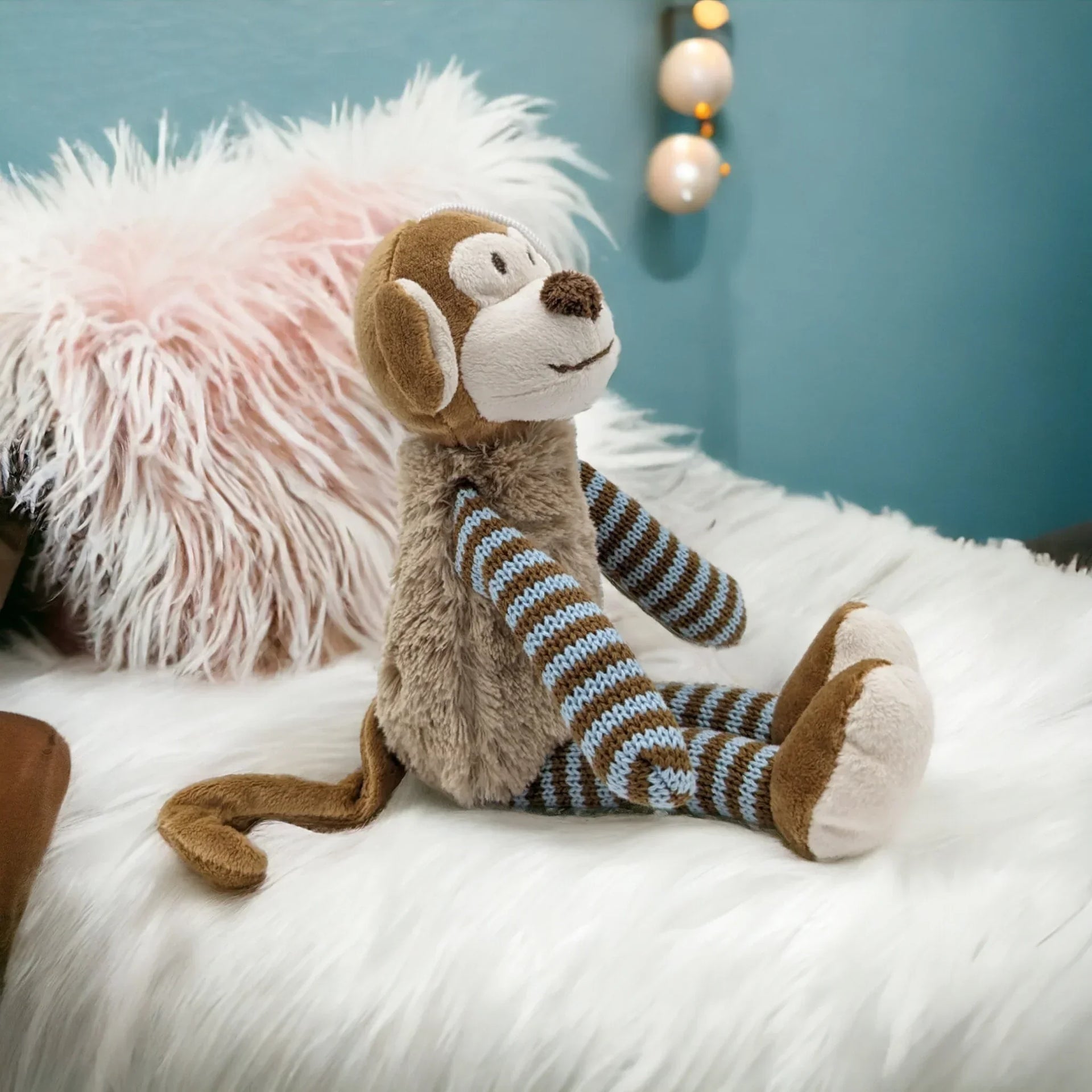 Cute plush monkey with striped knit limbs, sitting on fluffy white rug for nursery décor