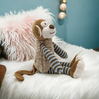 Cute plush monkey with striped knit limbs, sitting on fluffy white rug for nursery décor