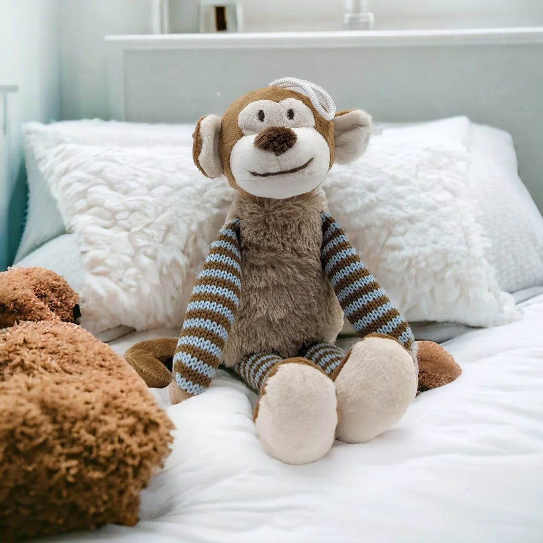 Cute plush monkey with striped sweater sitting on a cozy white bed, perfect for nursery decor.