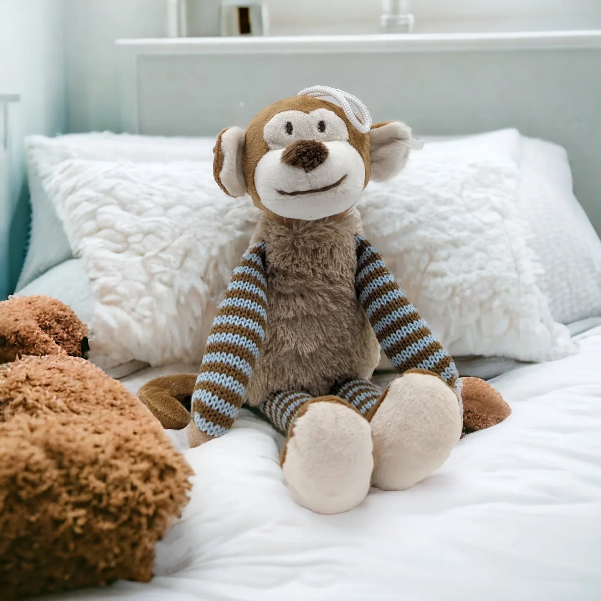 Cute plush monkey with striped sweater sitting on a cozy white bed, perfect for nursery decor.
