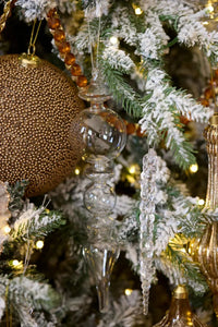 Clear glass Christmas ornaments on flocked tree with gold accents and warm lights