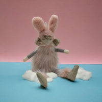 Pink plush bunny doll with fluffy fur, gray sleeves, and glittery boots, sitting on clouds against pink and blue background