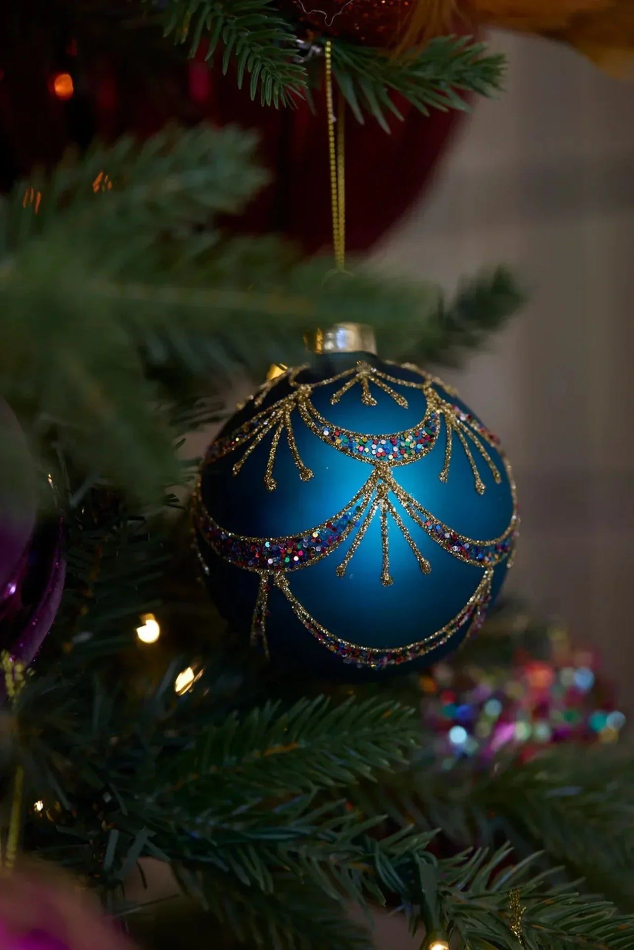 Elegant blue Christmas ornament with gold glitter swirls and colorful sequins on a tree