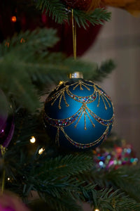 Elegant blue Christmas ornament with gold glitter swirls and colorful sequins on a tree