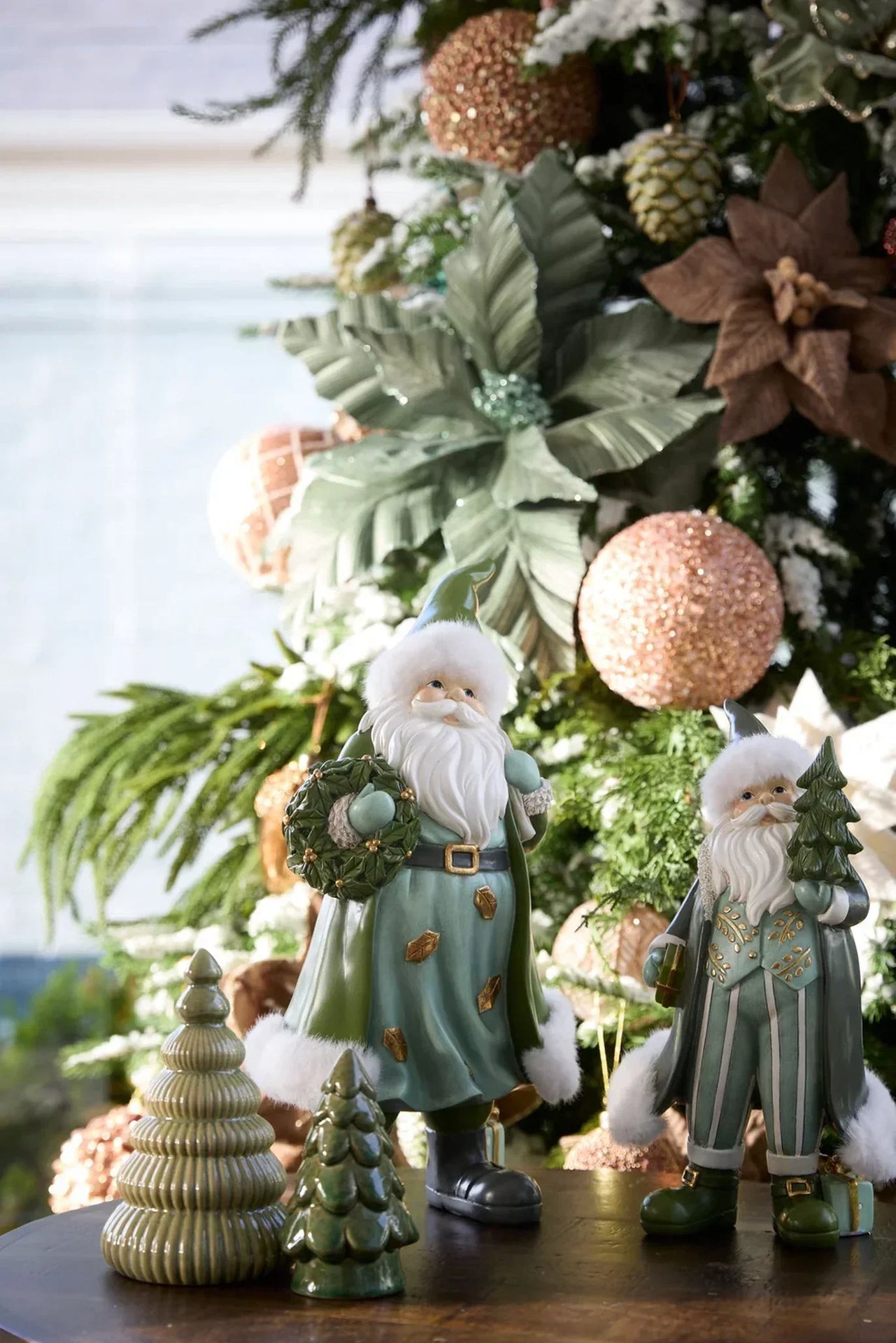 Green Santa figurines with wreath and tree, festive Christmas decor by a decorated tree