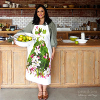 Woman wearing floral apron with apple blossoms, holding fruit bowl in rustic kitchen, home décor accessory