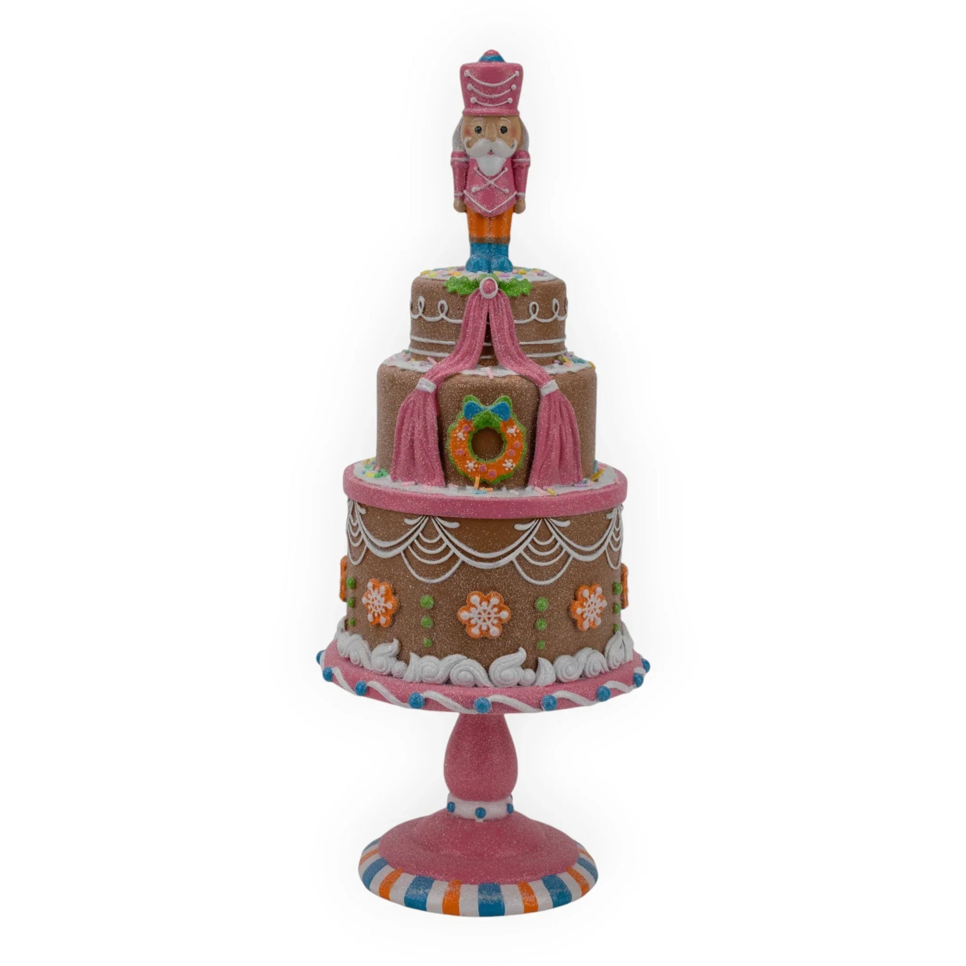 Pink nutcracker atop glittery gingerbread cake stand with festive wreath and snowflakes, holiday home decor