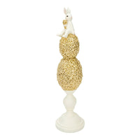 White bunny figurine perched atop gold floral egg stack on pedestal, elegant home décor accent