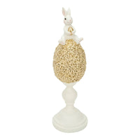 White bunny holding gold egg atop floral gold egg on pedestal, Easter home décor accent piece