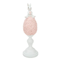 White bunny figurine holding pink egg, perched atop floral-textured pink egg on white pedestal base