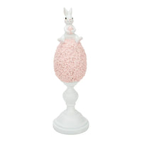 White bunny figurine holding pink egg, perched atop floral-textured pink egg on white pedestal base