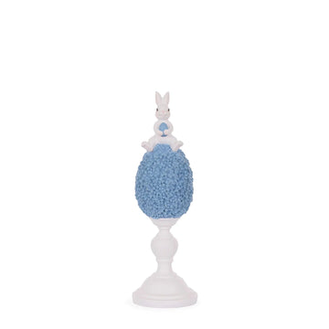 White bunny holding blue egg atop floral egg on pedestal, Easter home decor