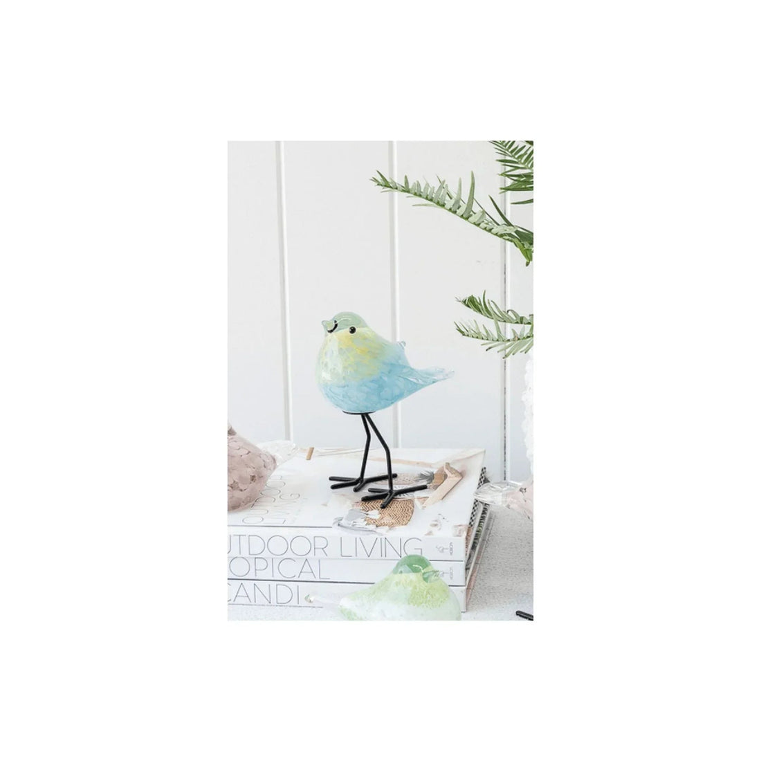 Pastel blue and green glass bird figurine with black wire legs, styled on books for home décor
