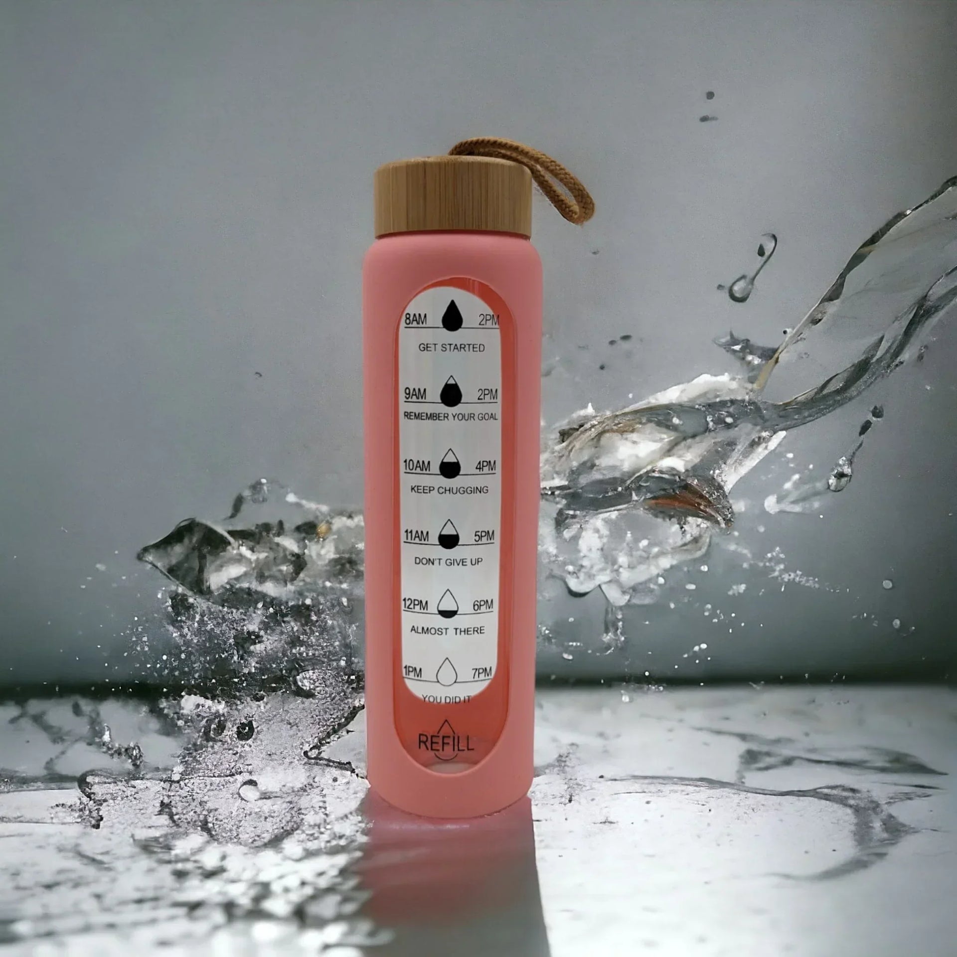 Pink motivational water bottle with time markers and bamboo lid, splashing water on marble surface