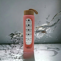 Pink motivational water bottle with time markers and bamboo lid, splashing water on marble surface