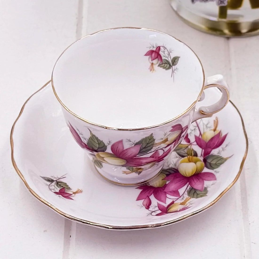 Elegant vintage teacup and saucer with pink fuchsia floral design and gold trim, perfect for afternoon tea.