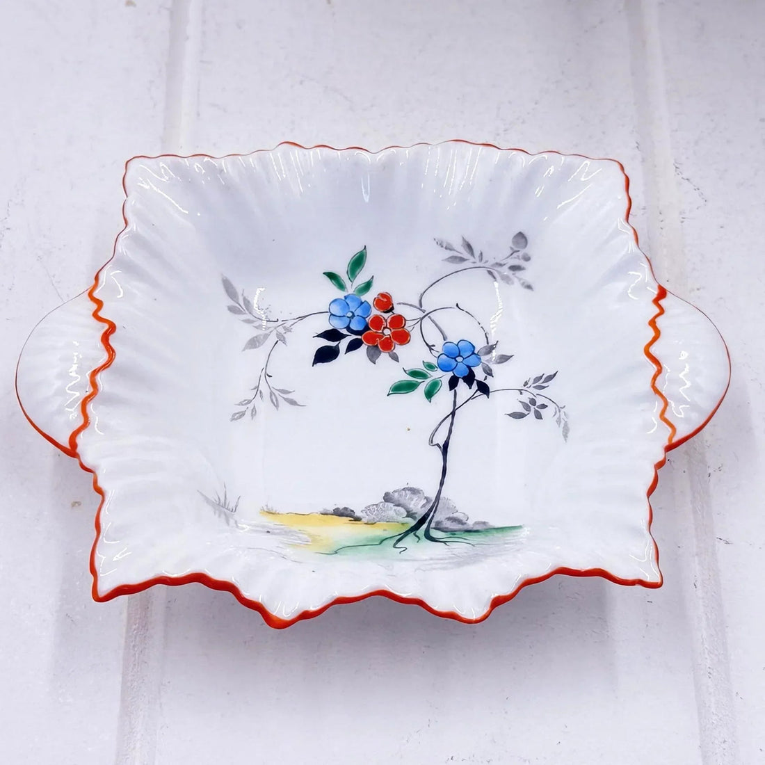 Vintage ceramic dish with hand-painted blue and red flowers, scalloped edge, and orange trim for home décor