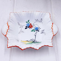 Vintage ceramic dish with hand-painted blue and red flowers, scalloped edge, and orange trim for home décor