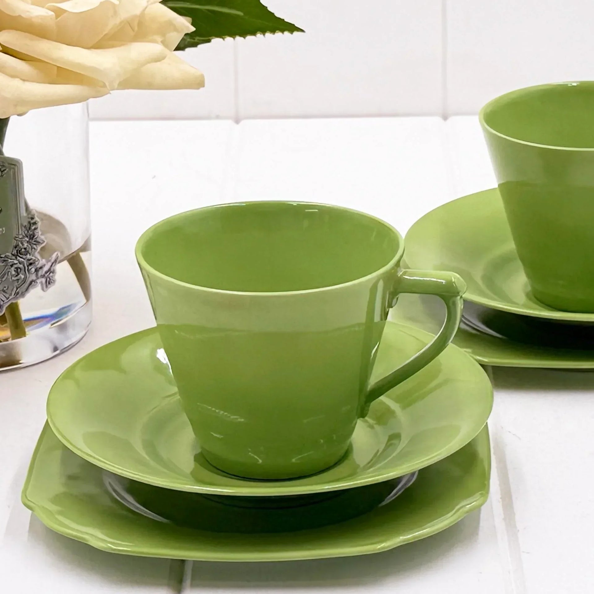 Vibrant green ceramic teacup and saucer set with matching plate, styled beside a white rose for elegant home décor.